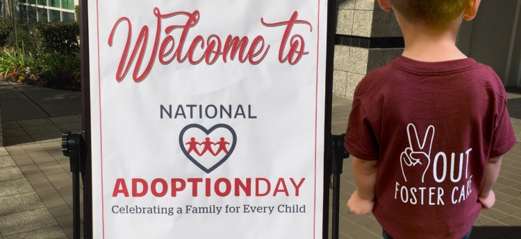 Sign for National Adoption Day next to a child wearing a shirt that says Peace Out Foster Care